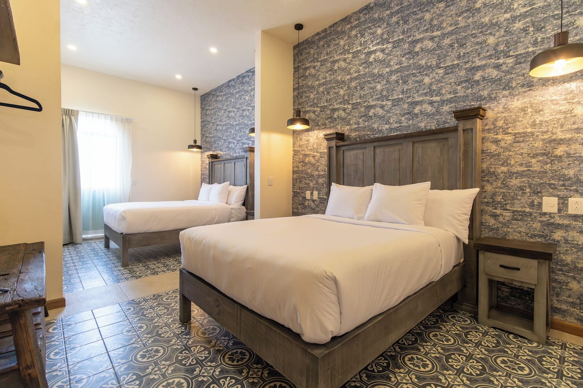 A hotel room with two beds, a wooden headboard, patterned floor tiles, and a textured wall.
