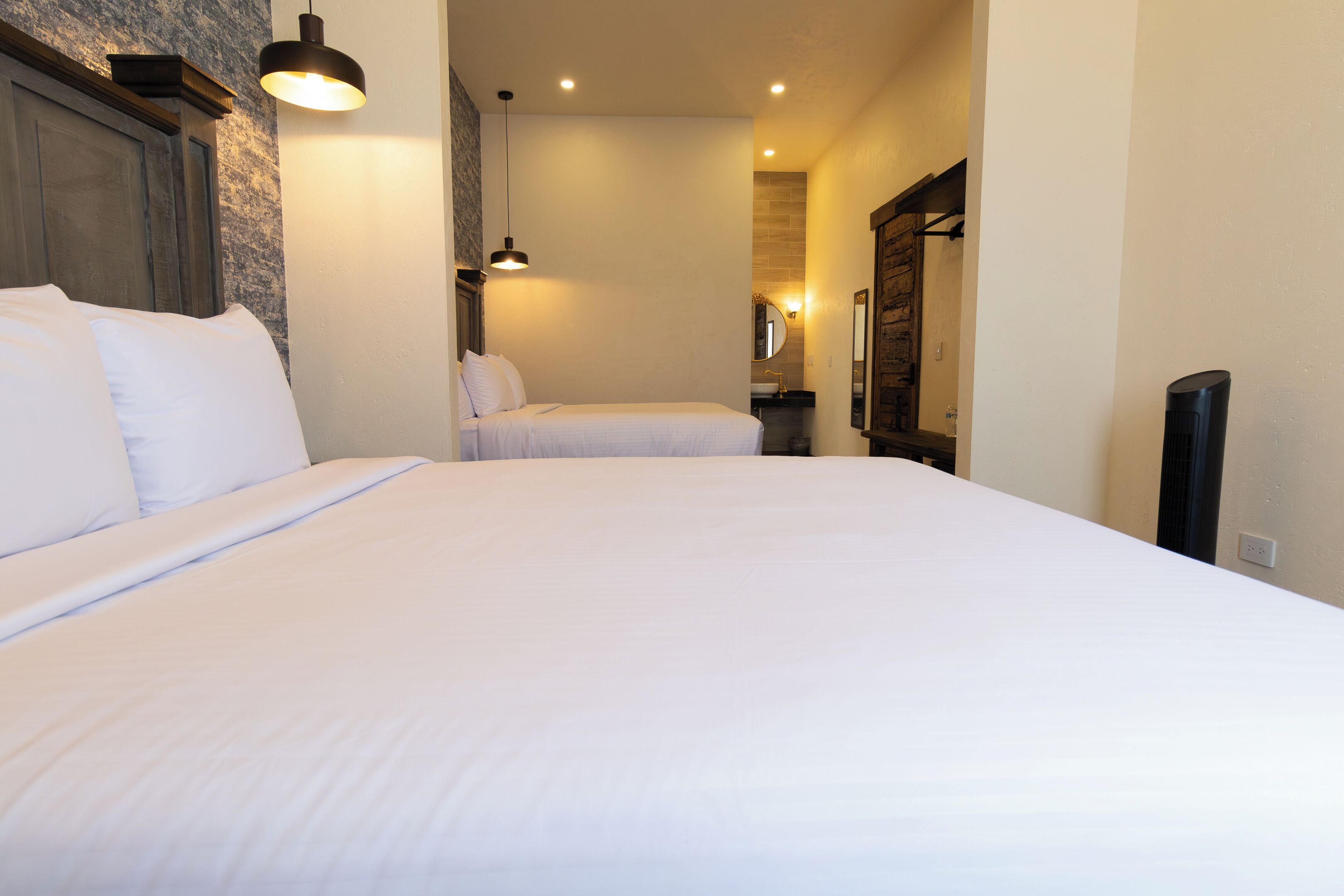A hotel room with two beds, a wooden headboard, a wall-mounted mirror, and a hanging light fixture.
