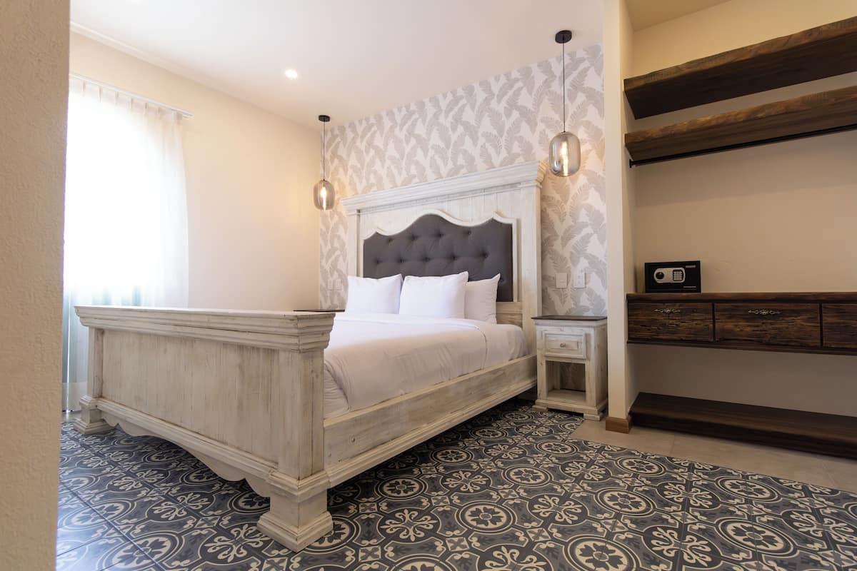 A bedroom with a large bed, a nightstand, a dresser, patterned floor tiles, and a decorative wall.