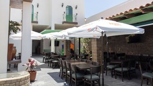 Eine Terrasse im Freien mit Tischen, Stühlen und Sonnenschirmen, daneben eine Backsteinmauer.