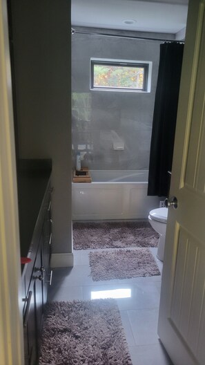 A bathroom with a bathtub, toilet, and a window. There are two rugs on the floor. - Storied Two Bedroom in the heart of the Sleeping Bear Sand Dunes (Empire)