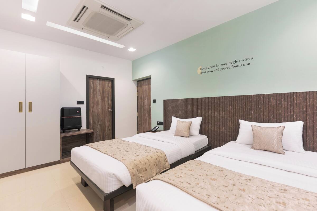 A hotel room with two beds, a wardrobe, a desk with a computer, and a wall with a motivational quote.