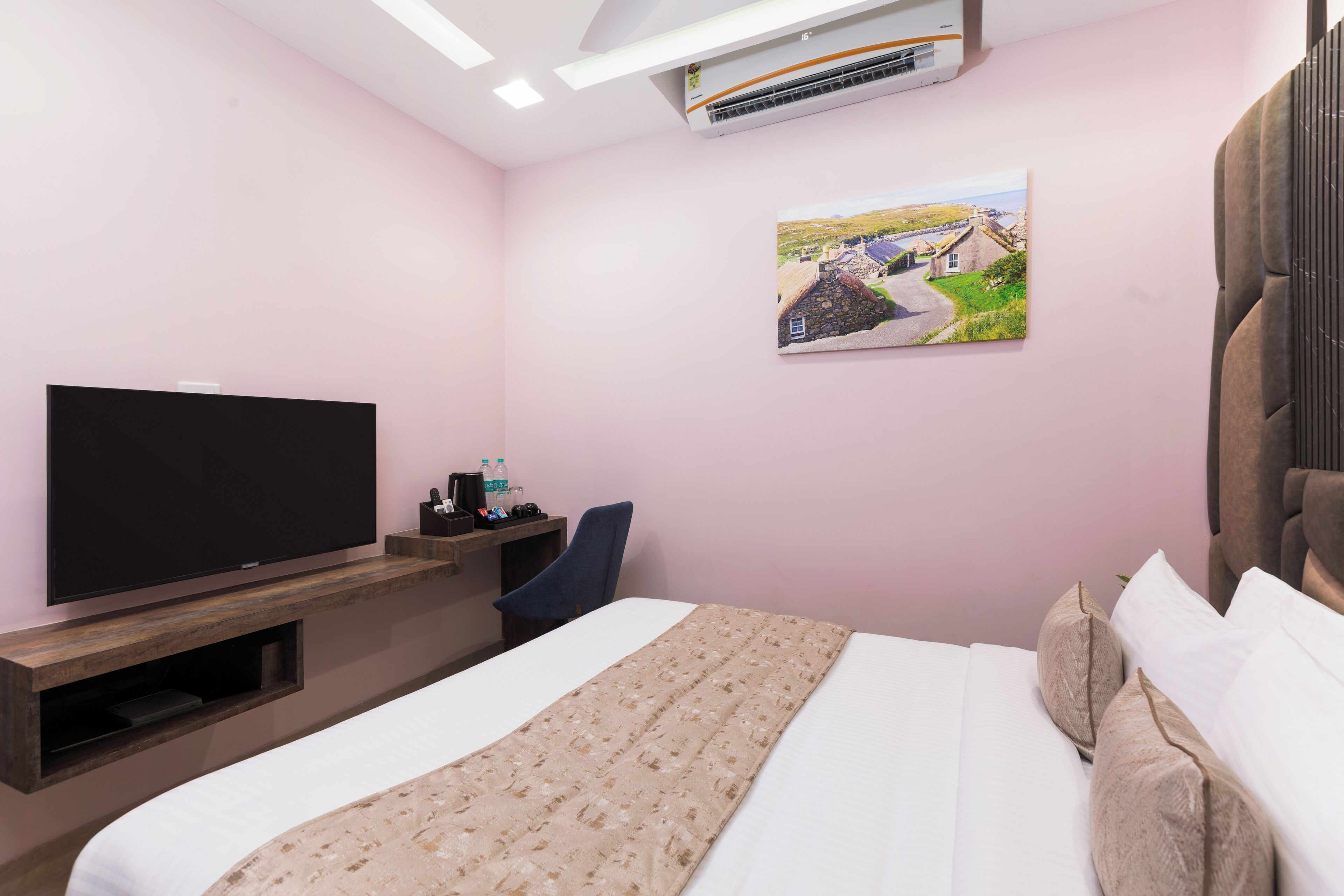 Ett hotellrum med en säng, en platt-TV, ett skrivbord med en stol och en luftkonditioneringsanläggning.