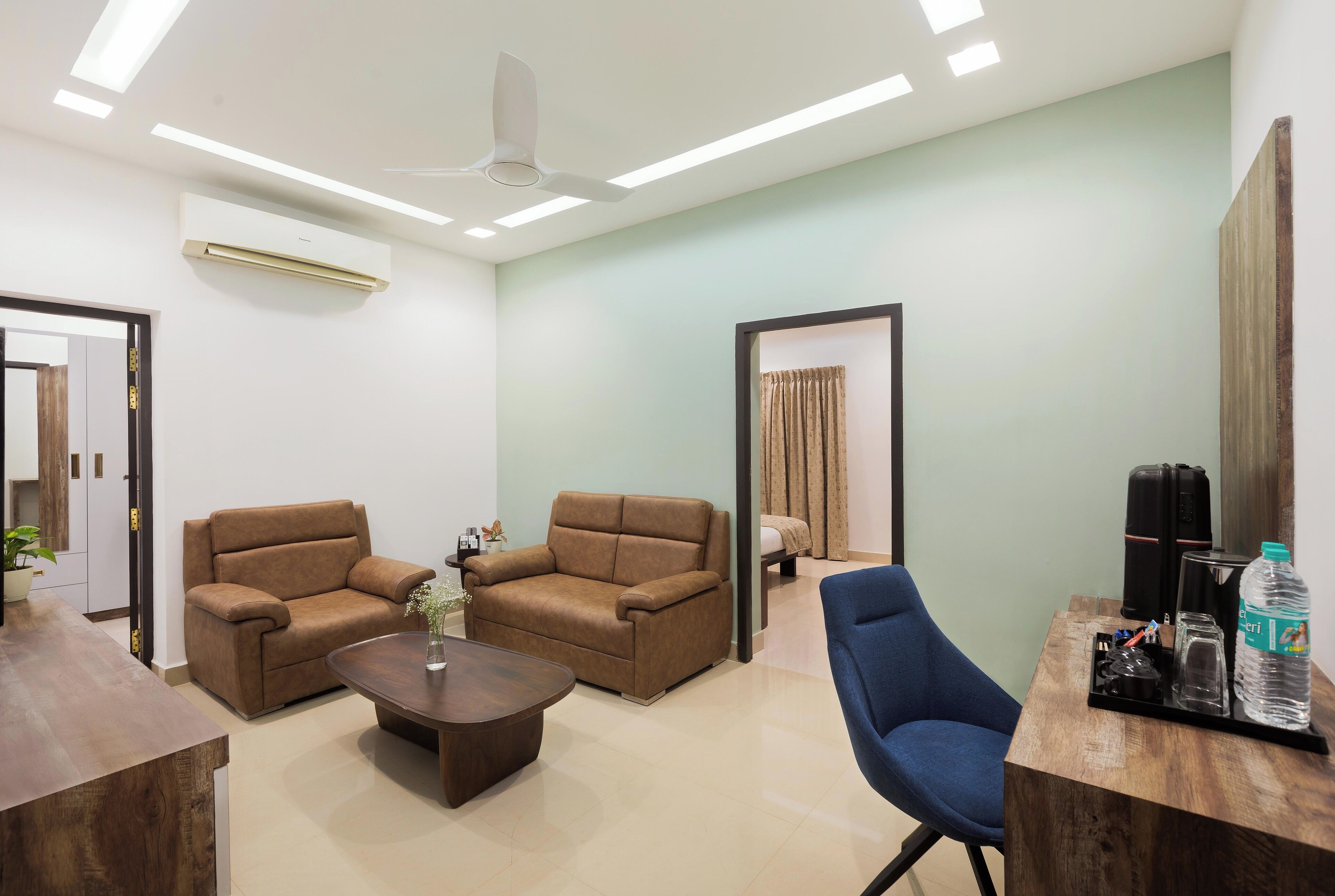 A modern room with two brown sofas, a blue chair, a wooden coffee table, and a desk with a water bottle.