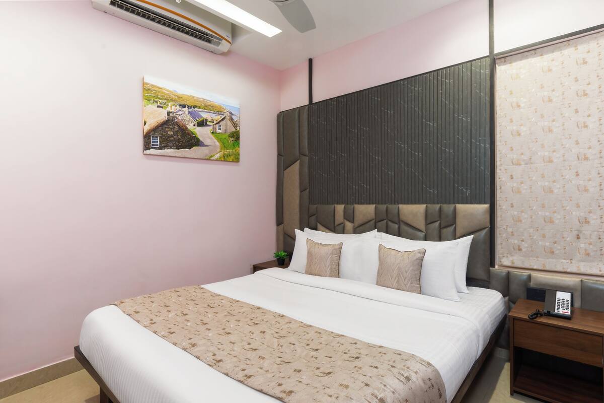 A bedroom with a bed, a nightstand, a telephone, a picture on the wall, and a window with blinds.
