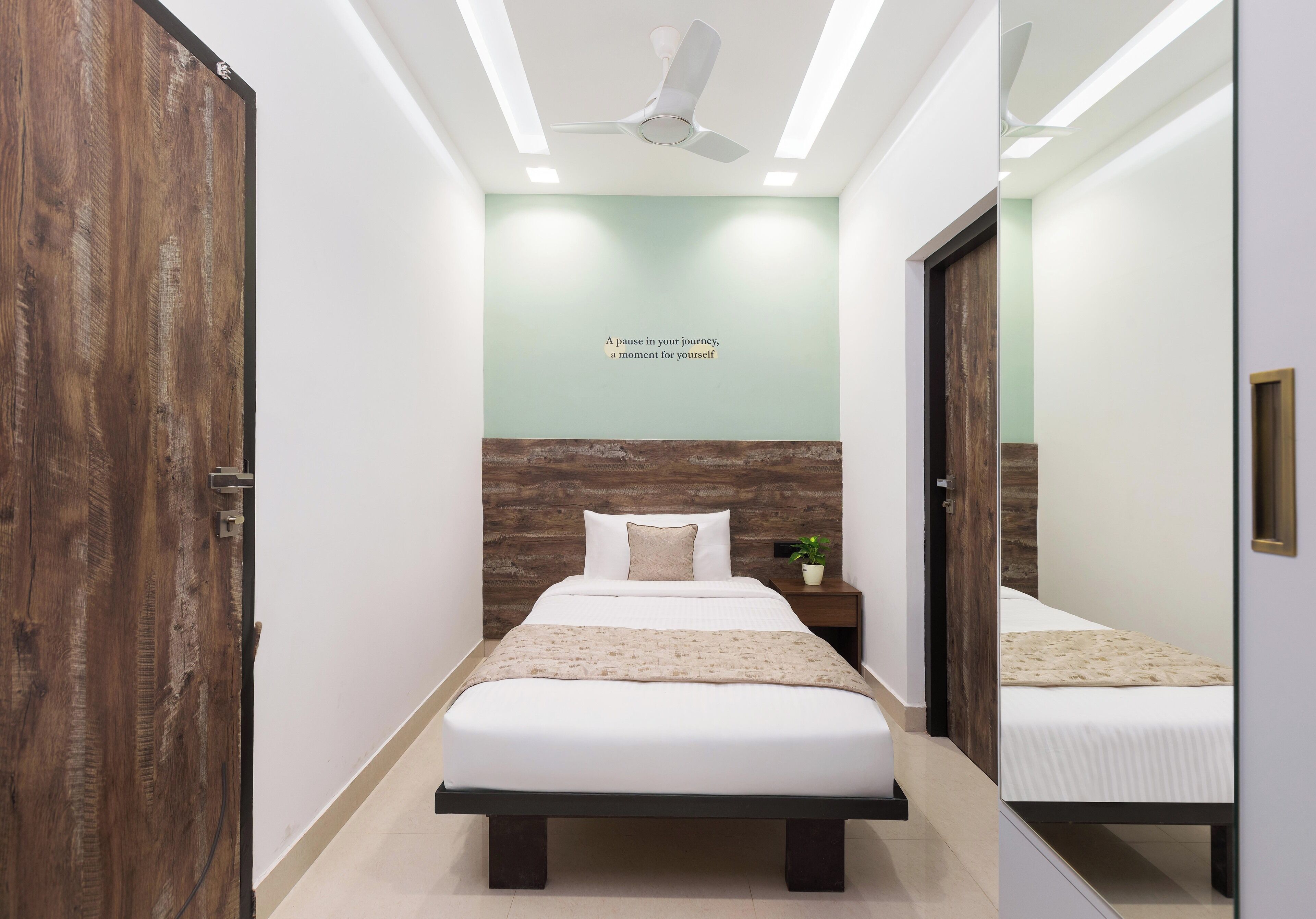 A modern bedroom with a large bed, a ceiling fan, and a motivational quote on the wall.