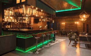 A bar area with a wooden bar counter, multiple stools, and a variety of bottles and glasses. - KAIRA PARK (Chennai)