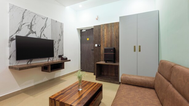 A modern living room with a flat-screen TV mounted on a marble wall, a wooden coffee table, a brown leather sofa, and a wardrobe with a dark wood finish.