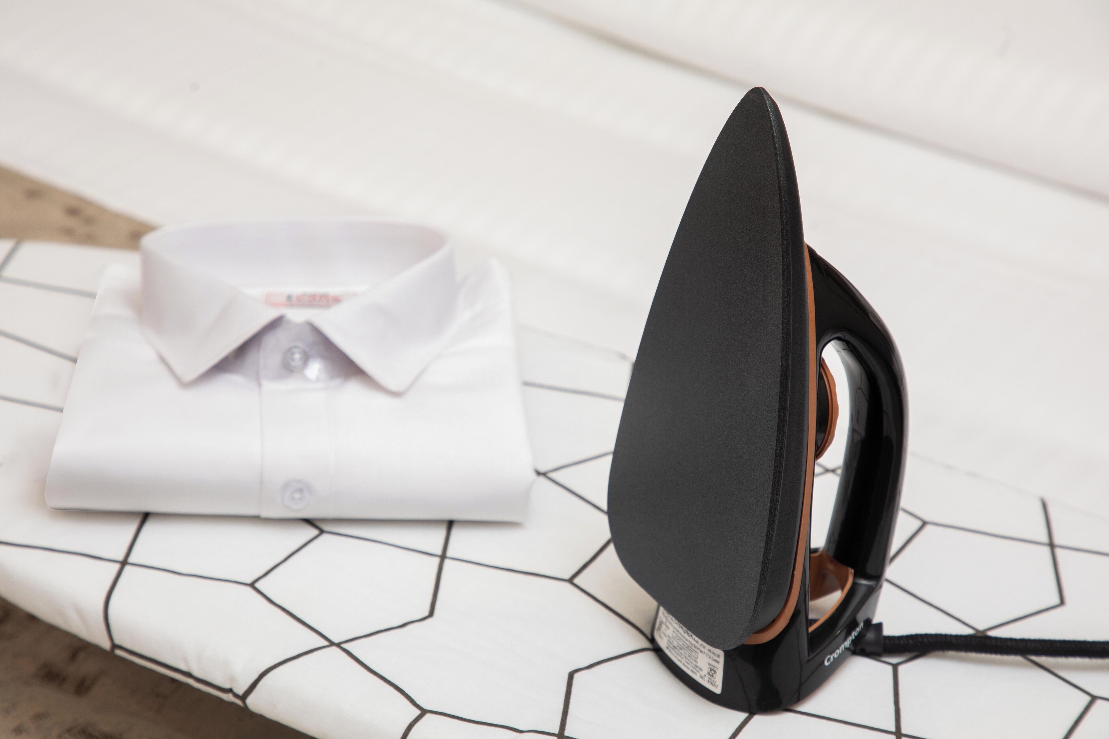 A neatly folded white shirt on a bed with a black iron on a white and black geometric-patterned bedspread.