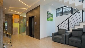 A modern lobby with a reception desk, elevators, a staircase, and a seating area. - KAIRA PARK (Chennai)