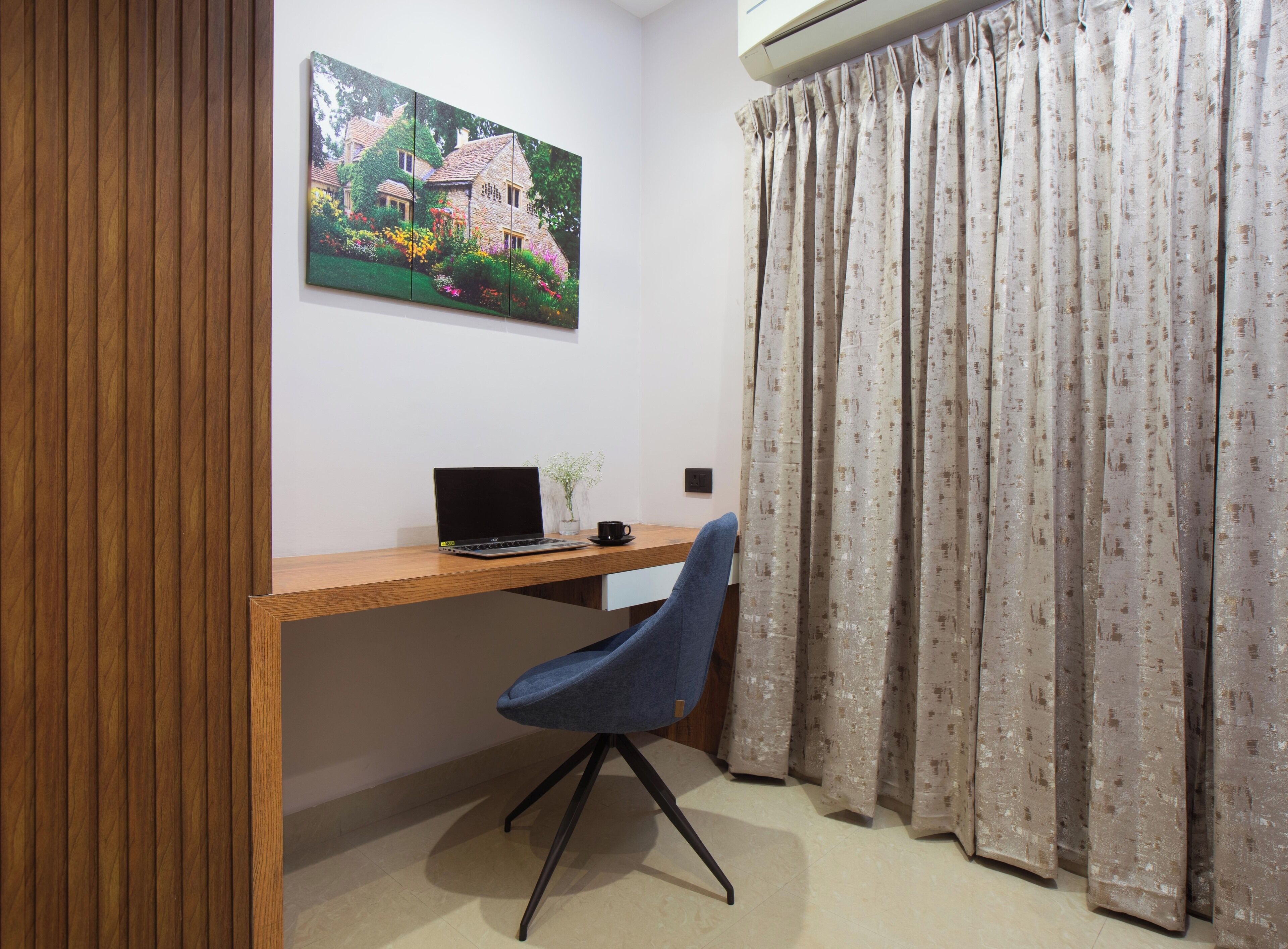 A room with a wooden desk, a laptop, a chair, a painting, and a curtain.