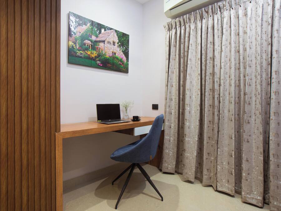 A room with a wooden desk, a laptop, a chair, a painting, and a curtain.