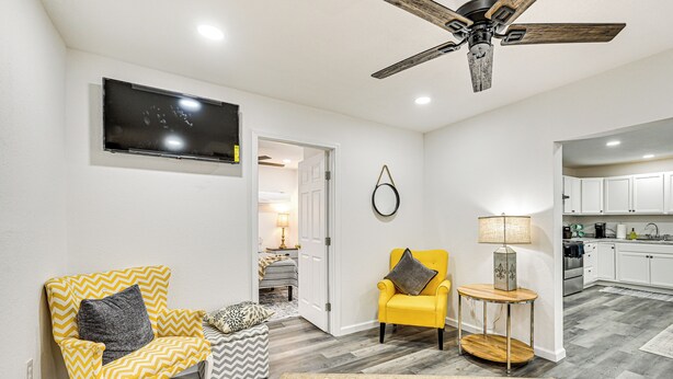 A living room with a ceiling fan, a TV mounted on the wall, a yellow armchair, a small round table with a lamp, and a patterned rug. - 1 Mi to Dtwn: Family Home w/ Porch in Brownwood (Brownwood)