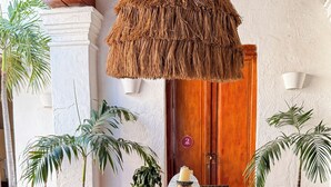 A dining area with a long wooden table, wicker chairs, a hanging thatched light fixture, and potted plants.