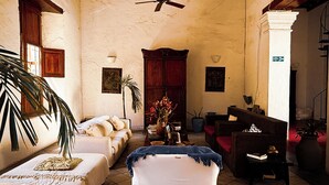 A spacious living room with a high ceiling, a ceiling fan, a wooden ceiling, a large window, a sofa, a coffee table, a potted plant, and a fireplace.