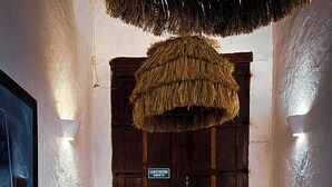 A room with a red carpet, a woven ceiling, a wooden door with a sign, and a table with decorative items.