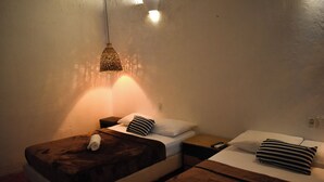 A room with two beds, each with a pillow and a blanket. There is a hanging light fixture above the beds.