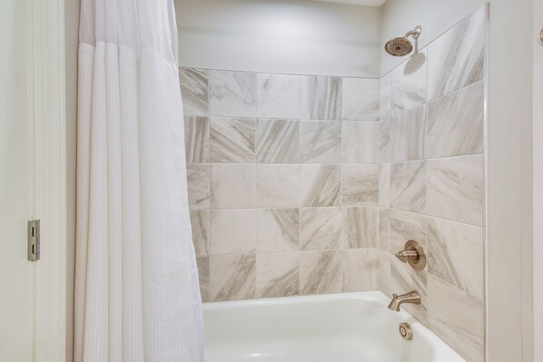 A bathroom with a bathtub, shower, and marble tiles. - Walkable Condo 3 Mi to Unicoi State Park (Helen)