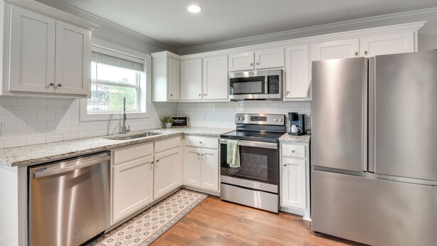 A modern kitchen with white cabinetry, stainless steel appliances, and a wooden floor. - < 1 Mi to Tubing: Sleek Condo in Downtown Helen (Helen)