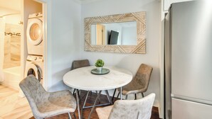 A modern kitchen with a stainless steel refrigerator, a round marble table with four chairs, and a washing machine in the background. - Steps to River + Shops: Downtown Helen Retreat! (Helen)