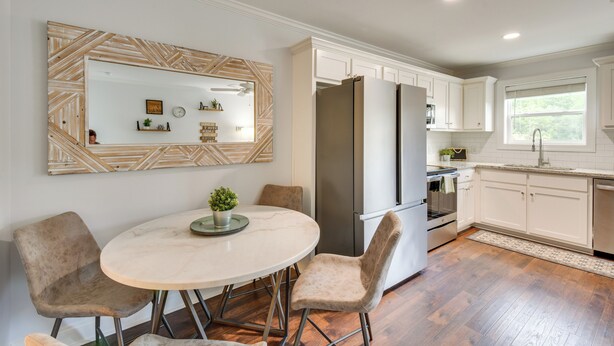A modern kitchen with white cabinets, a large refrigerator, and a dining area with a marble table and cushioned chairs. - Steps to River + Shops: Downtown Helen Retreat! (Helen)