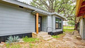 A house with a stone pathway leading to a wooden door, a small porch, and a large tree in the background. - Deck, Hot Tub & Lake View: Brownwood Home! (Brownwood)
