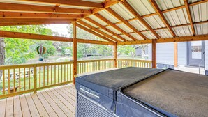 A covered outdoor deck with a hot tub, wooden railings, and a view of the surrounding area. - Deck, Hot Tub & Lake View: Brownwood Home! (Brownwood)