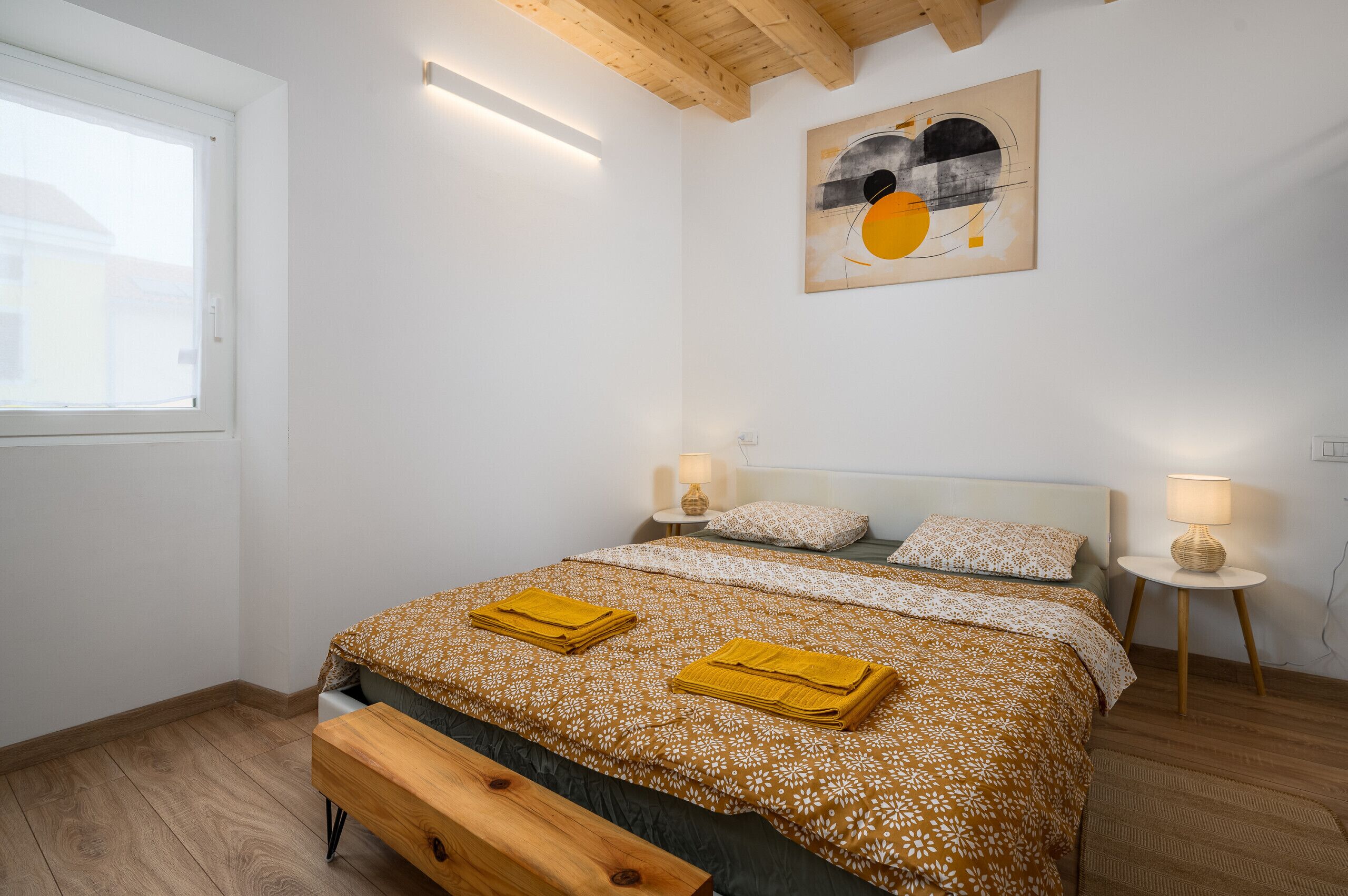 Une chambre à coucher avec un lit, des tables de chevet, une fenêtre et un tableau au mur.