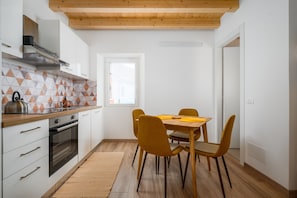 Una cocina moderna con armarios blancos, techo de madera y una zona de comedor con sillas amarillas.