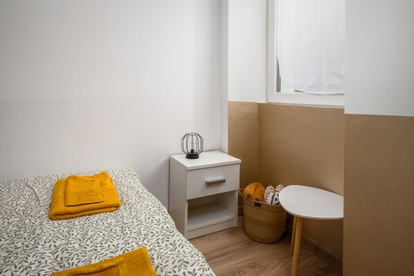 A bedroom with a bed, a nightstand, a small table, and a window.