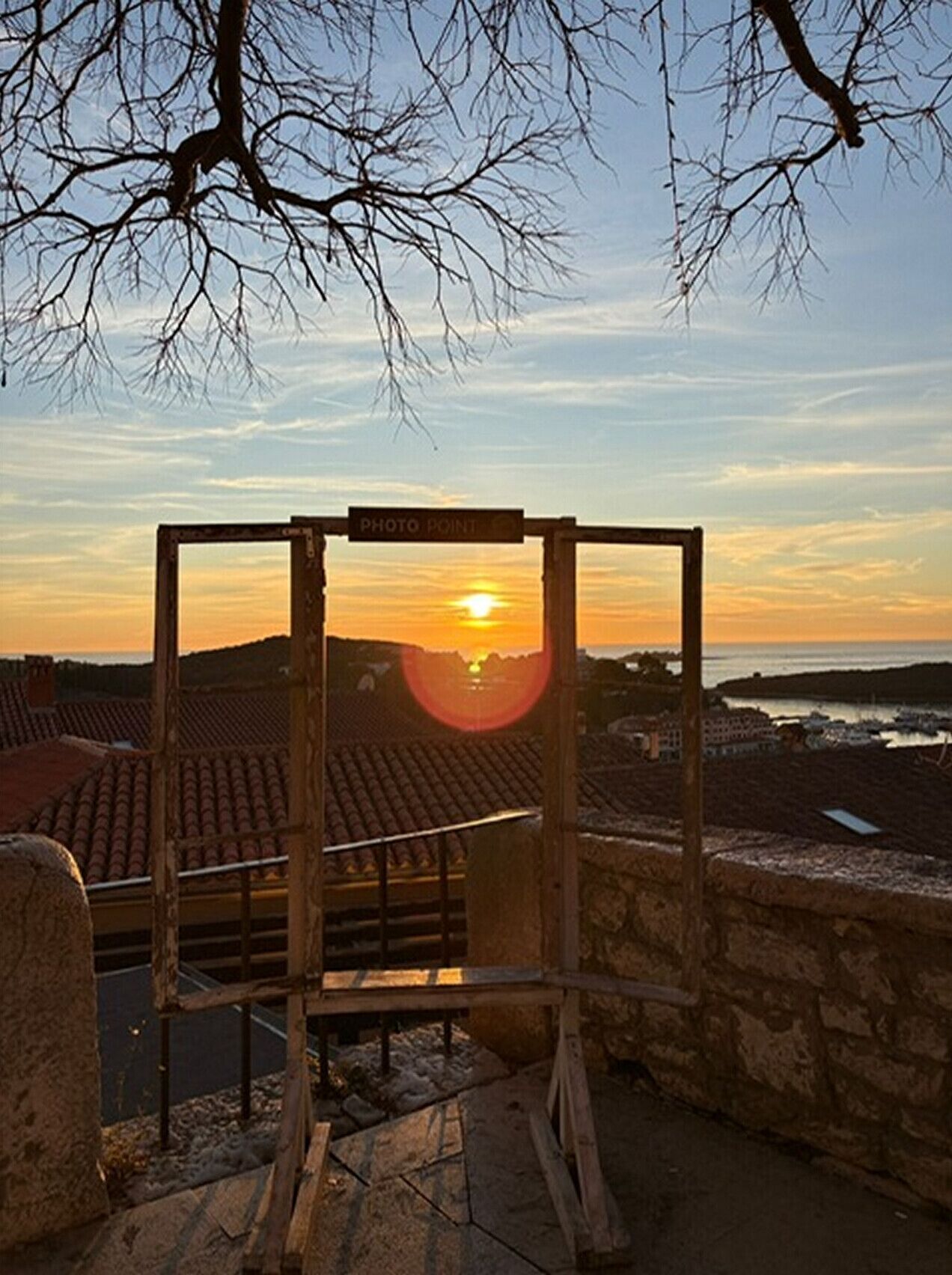 A wooden structure with a sign reading 'PHOTO POINT' in front of a sunset over a coastal town.