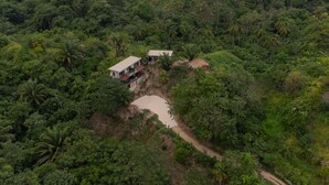 A remote, single-story house with a thatched roof, surrounded by dense tropical forest. - Casa Xué: Soul of Tayrona (La Poza)