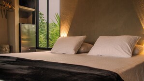 A bedroom with a bed, pillows, a black throw blanket, a nightstand, and a window with a view of greenery. - Casa Xué: Soul of Tayrona (La Poza)