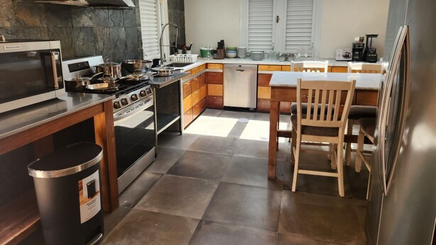 Una cocina moderna con estufa integrada, horno, microondas y lavavajillas. Hay una mesa de comedor de madera con sillas y un cubo de basura.