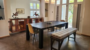 Un comedor con una mesa de madera oscura, sillas y un banco. Se observa una zona de cocina con una barra y elementos decorativos.