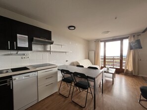 A compact kitchen with modern appliances, a dining area with a table and chairs, and a balcony with a view.