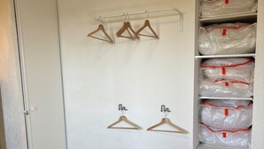 A room with a bed, a wardrobe with hangers, and shelves with packages.