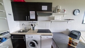 A compact kitchen with a washing machine, a coffee maker, and a clock on the wall.