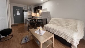 A compact room with a bed, a small table, a desk with chairs, and a kitchenette.