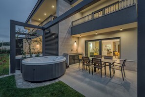 Une terrasse extérieure moderne dotée d’un jacuzzi, d’un espace repas et offrant une vue sur l’intérieur.