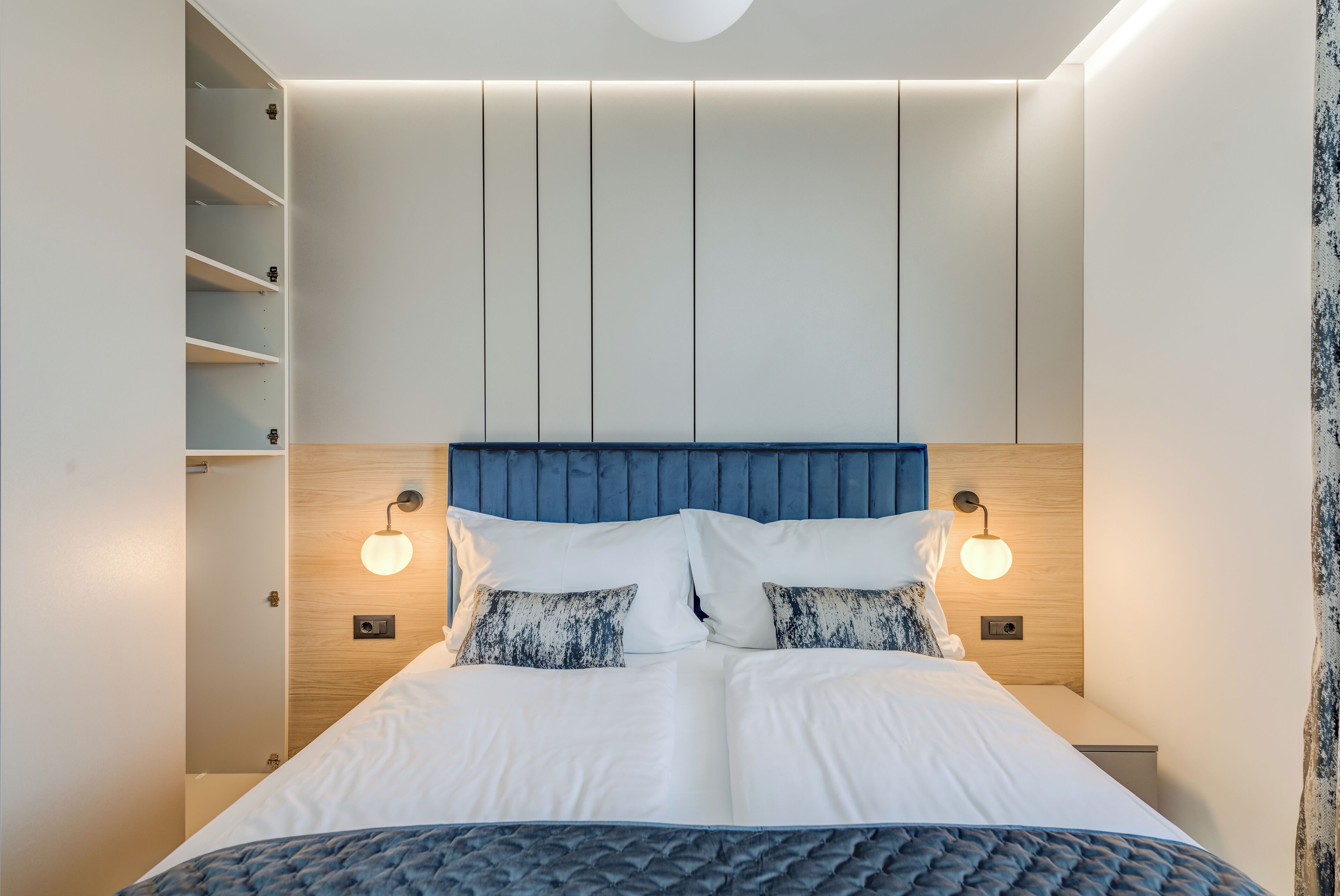Een moderne slaapkamer met een bed, twee nachtkastjes, een inbouwkast en wandlampen.