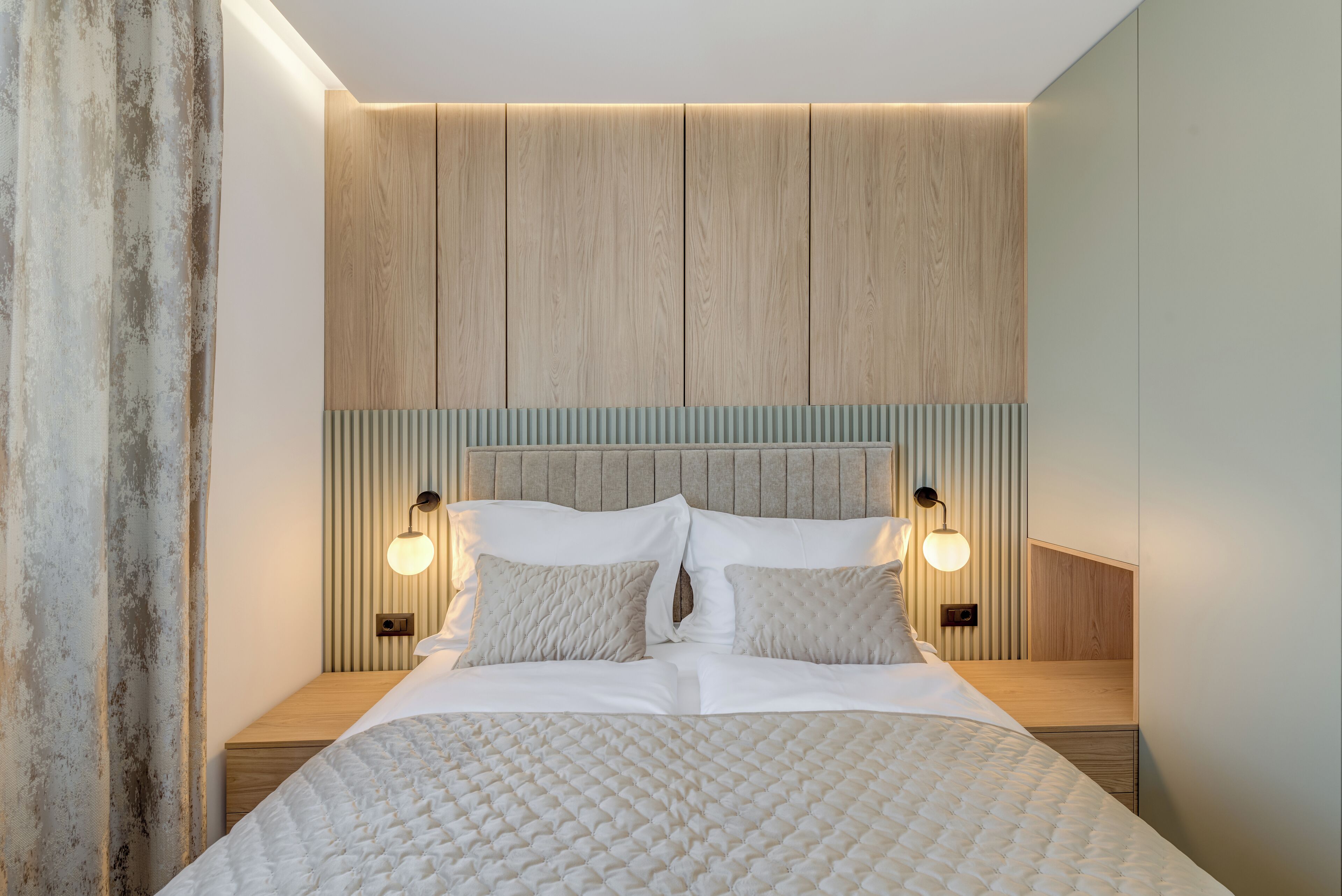 A modern bedroom with a large bed, wooden headboard, and two bedside lamps.