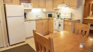 A compact kitchen with wooden cabinets, a white refrigerator, a microwave, and a stove. There is a wooden dining table with chairs. - 2 Bedroom Condo @ Banff Rocky Mountain Resort - June 14 to June 21, 2026 (Banff)