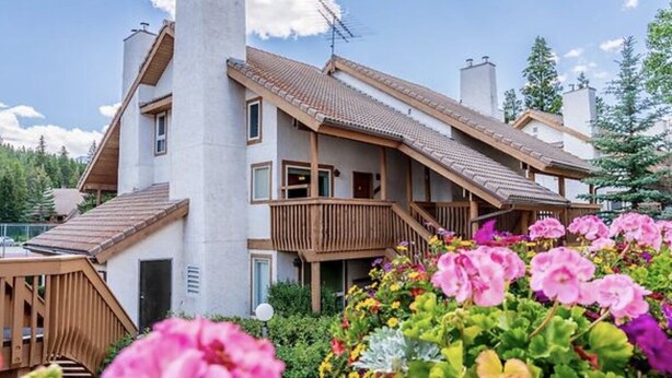 A multi-story building with a sloped roof, wooden balconies, and a garden with colorful flowers. - 2 Bedroom Condo @ Banff Rocky Mountain Resort - June 14 to June 21, 2026 (Banff)