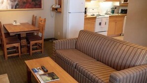 A compact living space with a wooden dining table, a patterned sofa, and a kitchenette in the background. - 2 Bedroom Condo @ Banff Rocky Mountain Resort - June 14 to June 21, 2026 (Banff)