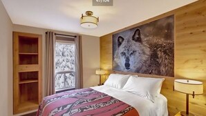 A hotel room with a large bed, a window with curtains, a wooden headboard, and a wall-mounted painting of a wolf. - 2 Bedroom Condo @ Banff Rocky Mountain Resort - June 14 to June 21, 2026 (Banff)