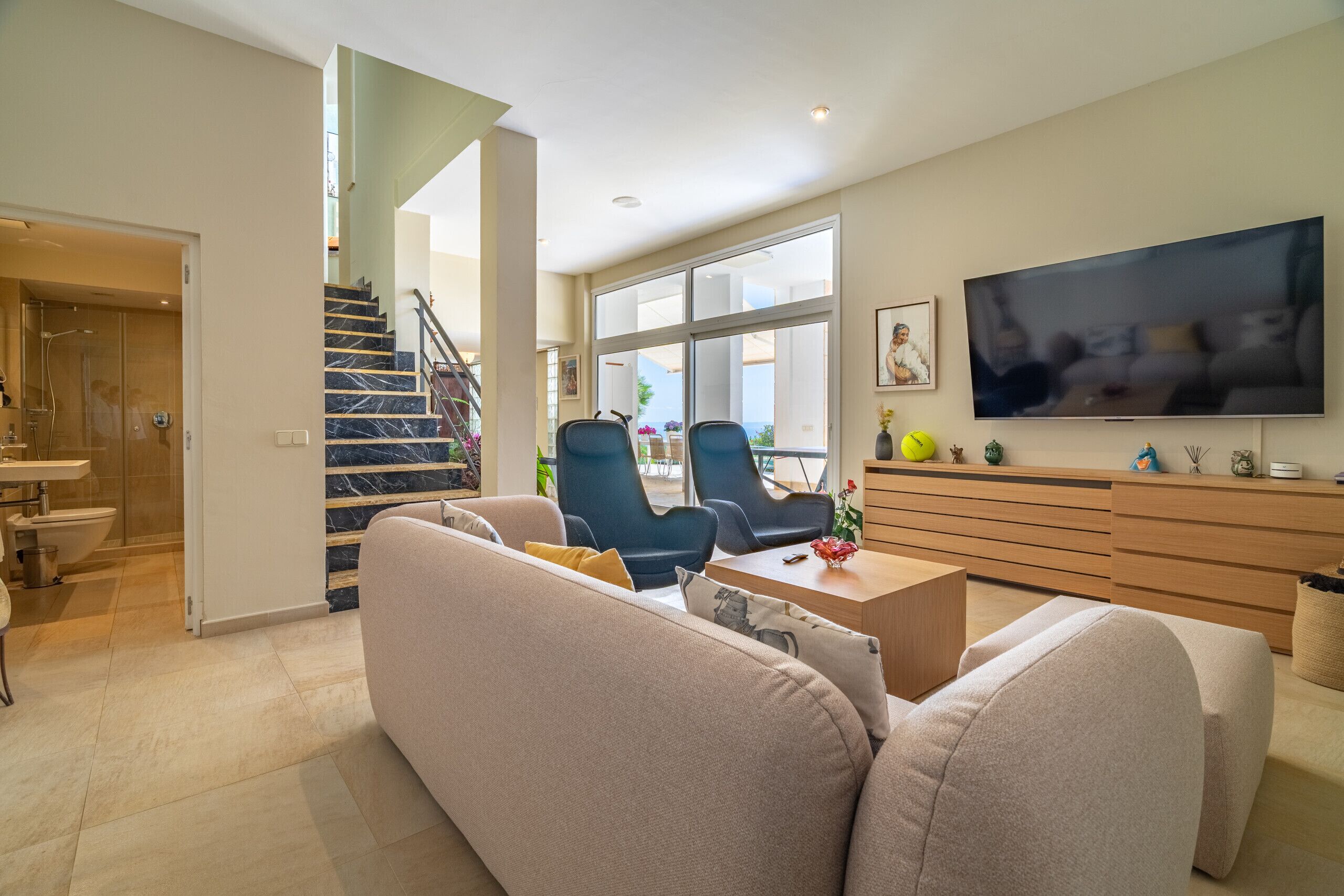 Een moderne woonkamer met een trap, een flatscreen televisie en een eethoek.