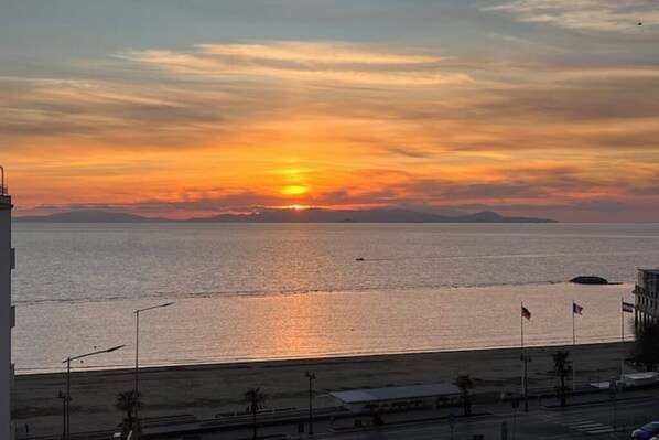 Solnedgang over vand med udsigt til strand og vej med flag.