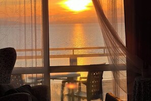 Et værelse med udsigt til solnedgangen over havet, et bord og stole.