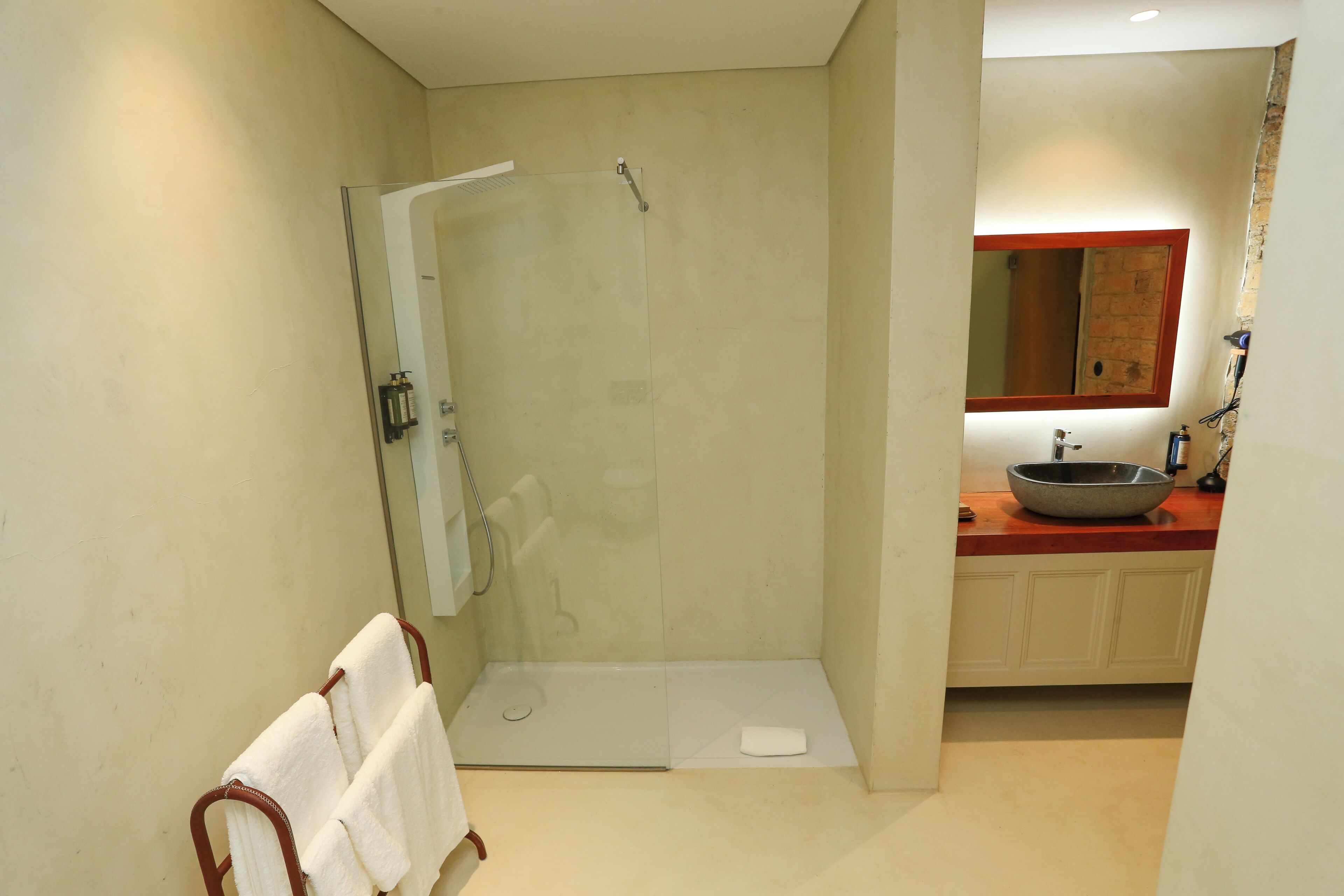 Une salle de bain moderne avec une douche à parois de verre, un lavabo blanc doté d’un receveur en pierre et un miroir avec un cadre en bois.